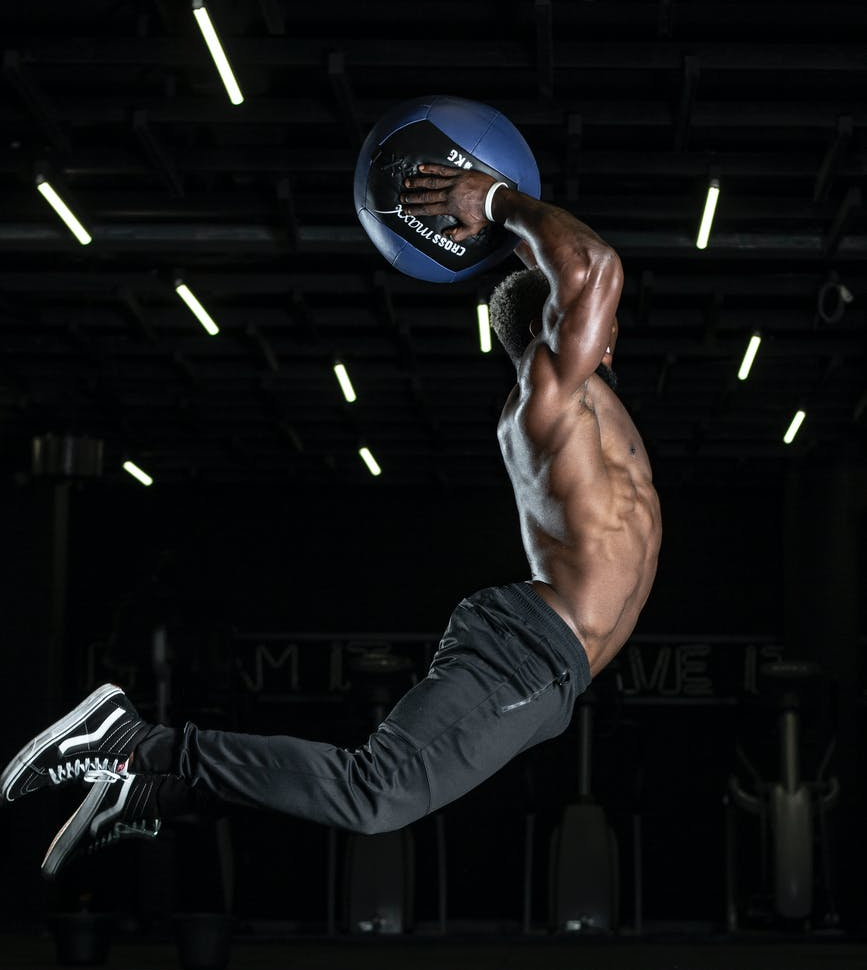 Man in air holding ball and showing fit body with muscles