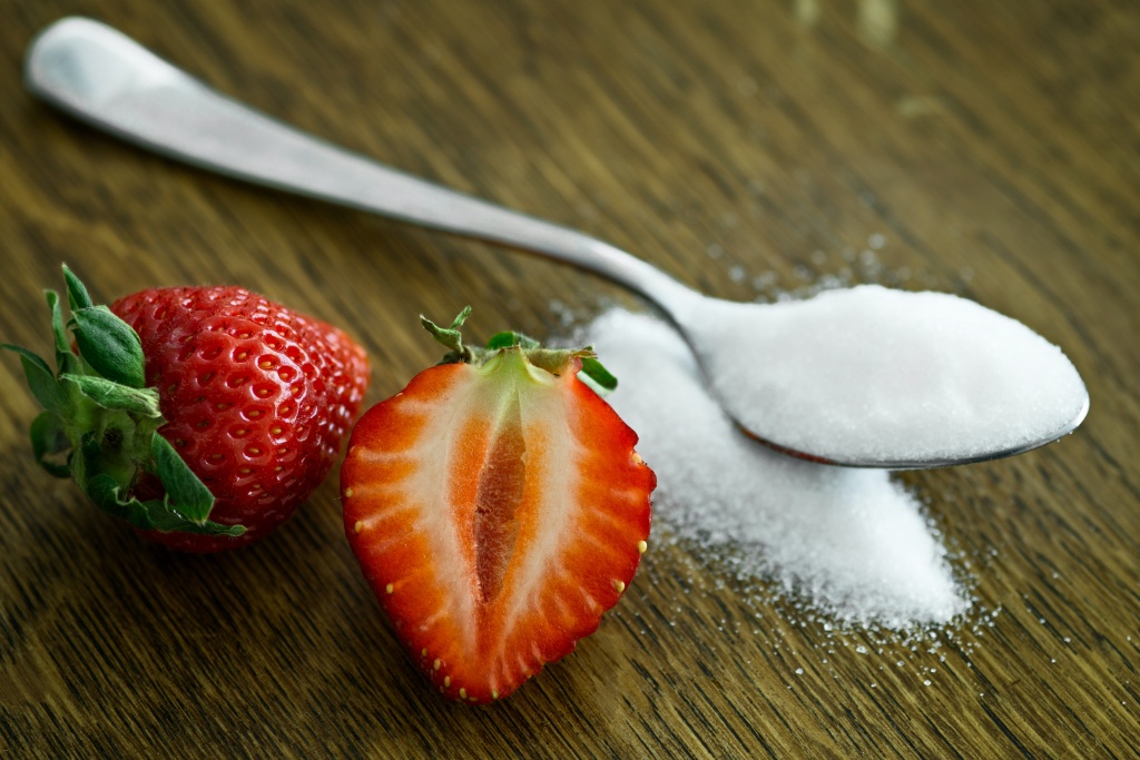 A spoon used in measuring sugar with straw berries in the background